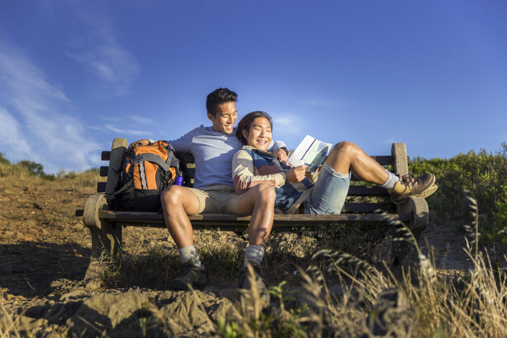 Happy gay hikers resting on bench. (Photo Credit: iStock)