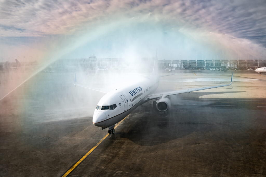 Fire hose salute with rainbow over United EQUAL Pride Flight UA 1991