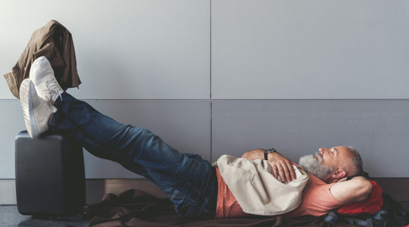 Older man sleeping or resting in an airport due to a flight cancellation or flight delay. (Photo credit: Olena Yakobchuk/Shutterstock)