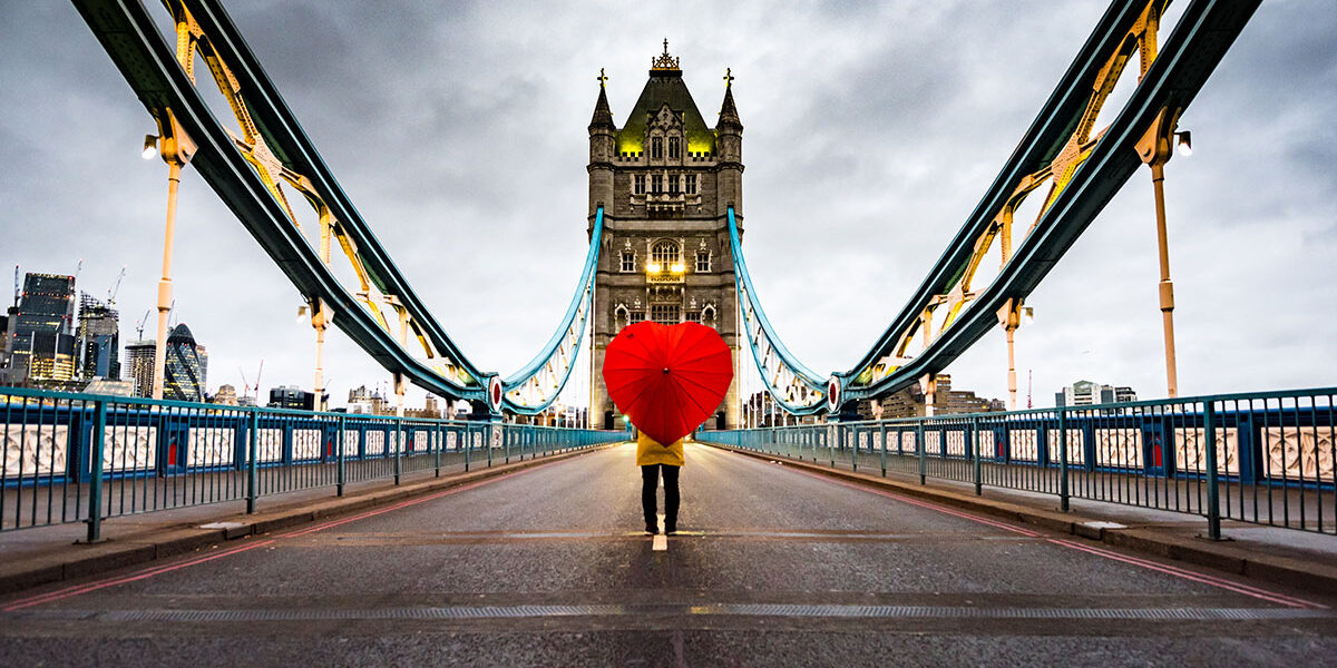 Reasons to visit Britain in 2022 - Girl standing on the Tower Bridge with a heart umbrella. (Photo Credit: Eachat / iStock)