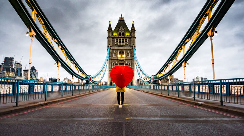 Reasons to visit Britain in 2022 - Girl standing on the Tower Bridge with a heart umbrella. (Photo Credit: Eachat / iStock)