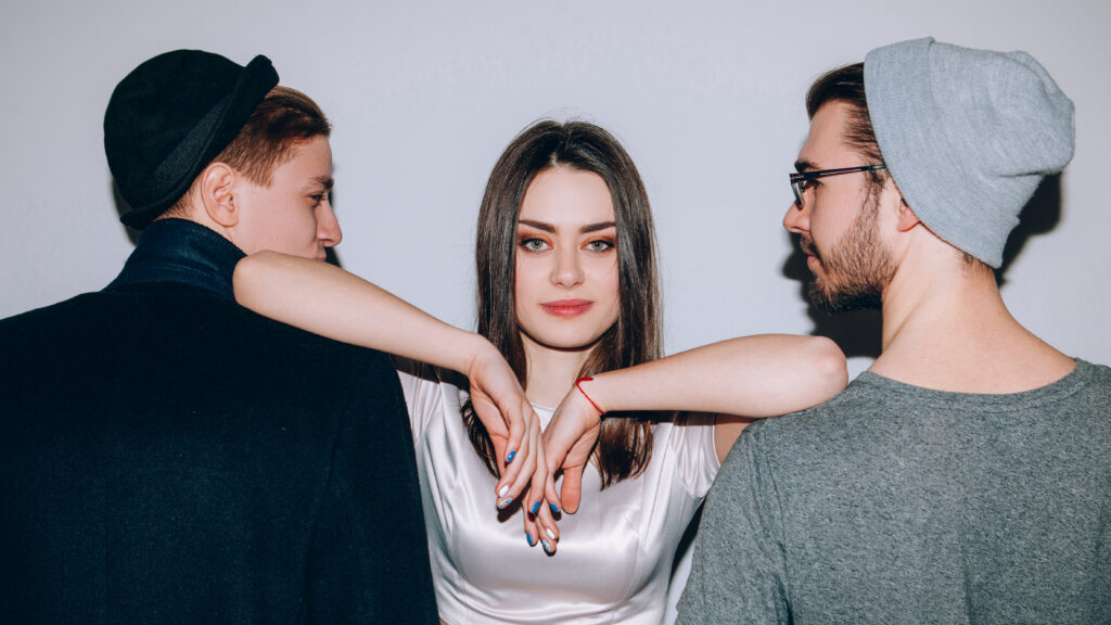 Polyamorous relationship. Modern partnership love. Confident woman dominating over two men. (Photo Credit: igor_kell / iStock)