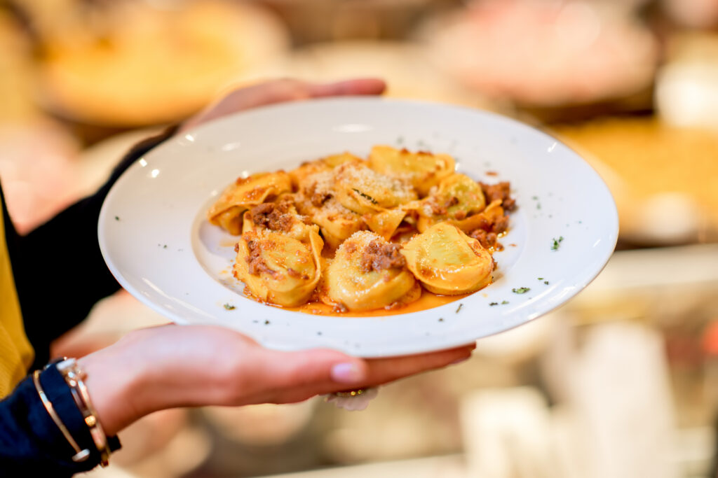 A plate with traditional ring-shaped pasta tortellini with bolognese in front of the food showcase background in Bologna, Italy (Photo Credit: RossHelen / Shutterstock)