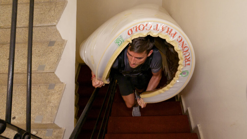 Ian and Joe struggle through the narrow stairway to deliver four mattresses to a local hotel in Vietnam. (Photo Credit: CBS)